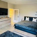 Schlafzimmer mit Bett, TV und Schrank. Tür führt in angrenzenden Raum.