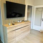 TV auf Holzwand, Sideboard mit Dekoration und Tür im Hintergrund.