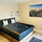 Schlafzimmer mit Bett, Wandbild und Sitzgelegenheit.