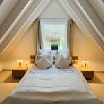 Schlafzimmer mit Dachschrägen, Bett, zwei Nachttischen und Fenster.