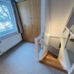 Treppenhaus mit Holztreppe, Garderobe und Fenster mit Blick auf Bäume.