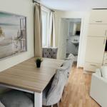 Essbereich mit Tisch, Stühlen und Küchenbereich. Wandbild zeigt Strand.