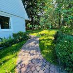 Pflasterweg führt durch grünen Garten zu weißem Haus