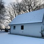 Wohnhaus mit schneebedecktem Dach und weißen Wänden in winterlicher Umgebung.