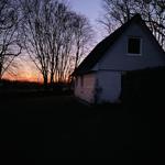 Haus mit Dach und Fenstern bei Sonnenuntergang hinter Bäumen.