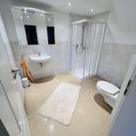 Badezimmer mit Dusche, Waschbecken und Toilette. Fliesenboden und Spiegel.