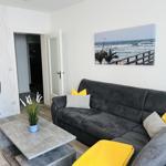 Wohnzimmer mit grauem Sofa, gelben Kissen und Küchenbereich im Hintergrund.