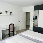 Schlafzimmer mit Bett, Schreibtisch, Kleiderschrank und Wandregal mit Pflanzen.