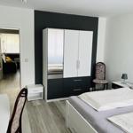 Schlafzimmer mit Bett, Kleiderschrank und Sicht auf Wohnzimmer.