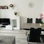 Essbereich mit Tisch, Stühlen und Pflanzen. Fernseher und Schrank im Hintergrund.