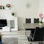 Esszimmer mit Tisch, Stühlen und Fernseher. Wanduhr und Pflanzen sind sichtbar.