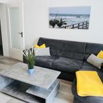 Wohnzimmer mit grauem Sofa, gelben Kissen und einem Tisch mit Pflanze.