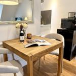 Holztisch mit Stühlen, Weinflasche und Zeitschrift. Küchenbereich mit Kühlschrank und Mikrowelle.