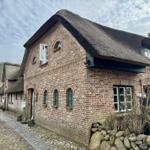 Traditionelles Backsteinhaus mit Strohdach und Steinmauer