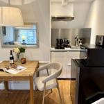 Essbereich mit Tisch, Stühlen und Spiegel. Küche mit Kühlschrank, Mikrowelle und Kochfeld.