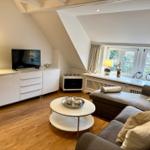 Wohnzimmer mit Sofa, TV und Fenster. Holzboden und weiße Möbel.