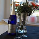 Blauer Sekt, zwei Gläser und Blumen auf Fensterbank.