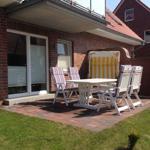 Terrasse mit weißem Tisch, Stühlen und Sonnenschirm. Hintergrund: roter Backsteinbau mit Fenstern.