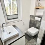 Badezimmer mit Waschbecken, WC und Dusche. Fenster mit Blick auf Bäume.