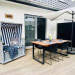 Terrasse mit Strandkorb, Tisch und Stühlen unter Sonnenschutz.