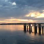 Sonnenuntergang über dem Wasser mit Pier und Booten im Hintergrund.
