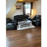 Wohnzimmer mit drei schwarzen Ledersitzen, weißem Couchtisch und Holzboden.