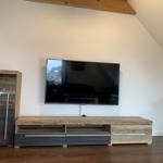 TV auf Wandhalterung, Holzregal und Pflanze im Raum