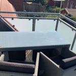 Terrasse mit Tisch und Stühlen, Glasgeländer und Blick auf Nachbarhäuser.