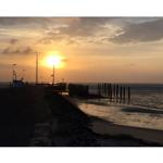 Sonnenuntergang am Hafen mit Booten und Steg im Wasser.