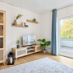 Wohnzimmer mit TV, Schrank und Balkontür. Holzboden und Pflanzen.