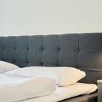 Doppelbett mit grauem Kopfteil und weißen Kissen