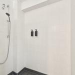 Dusche mit Duschbrause, Wandhalter und zwei schwarzen Flaschen.