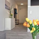 Vorraum mit Blumen und moderner Einrichtung. Hintergrund zeigt Flur und Tür.