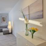 Wohnbereich mit Sofa, Beistelltisch und Stehlampe. Anrichte mit Blumen und Wandbildern.