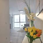 Vorraum mit Blumen, Blick in Wohnbereich mit Sofa und Fenster.