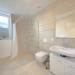Badezimmer mit Dusche, Waschbecken und Toilette. Fenster mit Jalousie.