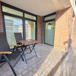 Terrasse mit Tisch und zwei Stühlen vor einer Glasfront.