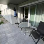 Terrace with table, two chairs, and blue umbrella. Glass door leads into the house.