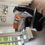 Living room with sofa, two chairs, and glass table. Access to balcony with view of greenery.