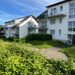 House with balconies and green garden area under blue sky.