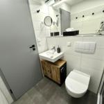 Badezimmer mit Waschbecken, Toilette und Spiegel. Holzunterschrank und graue Fliesen.