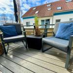 Terrasse mit zwei Sesseln, Tisch und Pflanzen. Hintergrund: Haus mit Dachfenstern.