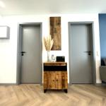 Eingangsbereich mit Holzschrank, zwei Türen und Sofa im Hintergrund.