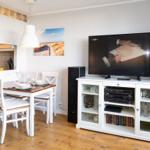 Dining area with table and chairs. TV on white cabinet with glass panels.