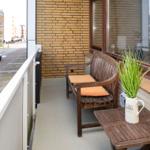 Terrace with wooden bench, orange cushions, and plant in white vase.