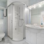 Badezimmer mit Dusche, Waschbecken und Toilette. Fliesenwand mit Mosaikstreifen.