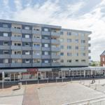 Modernes Mehrfamilienhaus mit Geschäften im Erdgeschoss und Terrassen auf den Stockwerken.