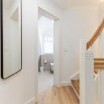 Haus mit Holztreppe und Spiegel. Im Hintergrund ist ein Badezimmer mit Toilette und Fenster.