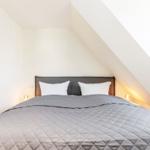 Schlafzimmer mit Dachschrägen und Bett mit grauer Bettdecke.