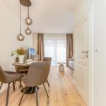 Essbereich mit Tisch, Stühlen und Hängelampen. Blick in Wohnbereich mit Sofa und Fenster.